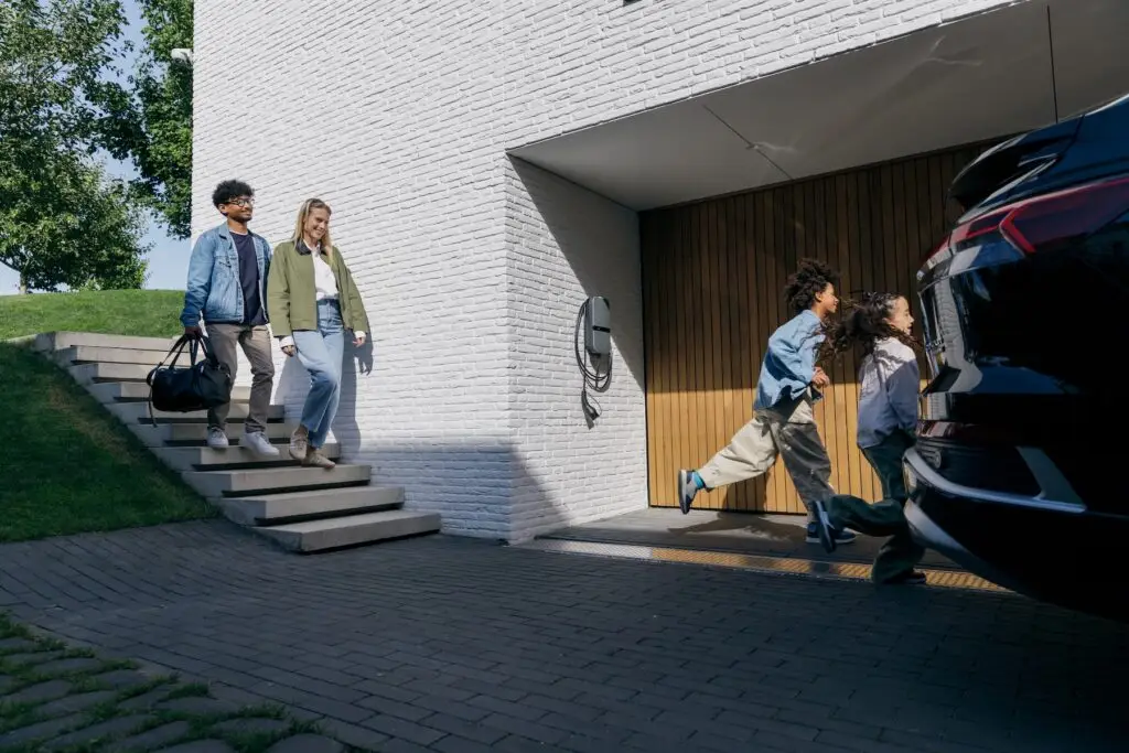 Laadstation bij garage ingang. Gezin loopt naar auto.